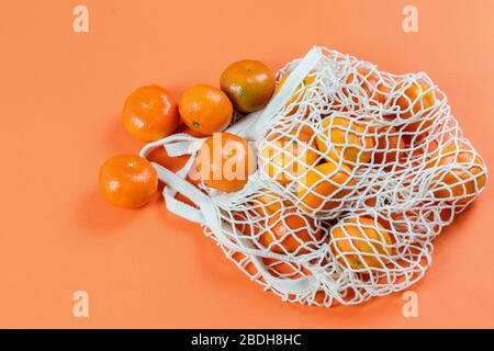 Gruppe von Mandarinen in der Saite Baumwollbeutel auf dem orangefarbenen Hintergrund isoliert. Kein Abfall, kein Kunststoffkonzept. Stockfoto