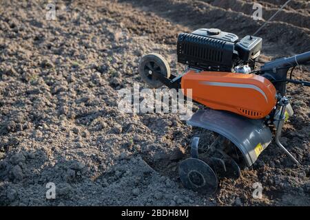 Kleine orange Pflügemaschine in den Händen eines Landwirts, der in schwarzem Boden anbaubar macht Stockfoto