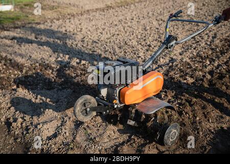 Kleine orange Pflügemaschine in den Händen eines Landwirts, der in schwarzem Boden anbaubar macht Stockfoto