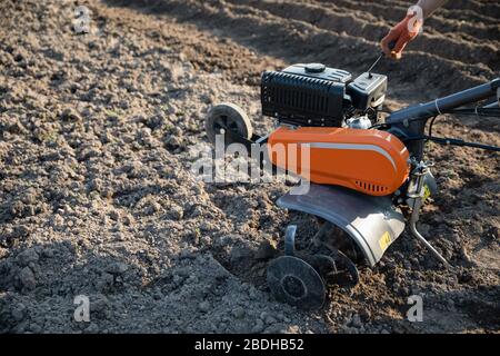 Kleine orange Pflügemaschine in den Händen eines Landwirts, der in schwarzem Boden anbaubar macht Stockfoto