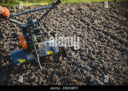 Kleine orange Pflügemaschine in den Händen eines Landwirts, der in schwarzem Boden anbaubar macht Stockfoto