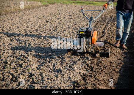 Kleine orange Pflügemaschine in den Händen eines Landwirts, der in schwarzem Boden anbaubar macht Stockfoto