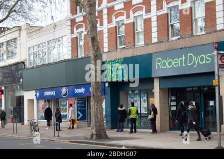 Käufer, die zwei Meter voneinander entfernt warten, um während der Covid-19-Pandemie, Chiswick, London UK, in einen Stiefel zu kommen Stockfoto