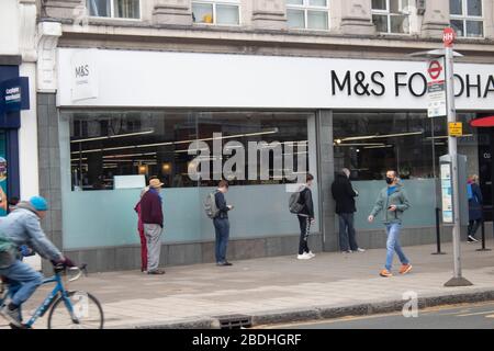 Käufer, die zwei Meter voneinander entfernt warten, um während der Covid-19-Pandemie in Chiswick, London UK, in Marks und Spencer Fuß zu fassen Stockfoto