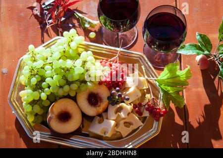 Zwei Gläser Rotwein und Käseplatte, frische Trauben, Pfirsiche und Beeren auf Holztisch. Außenstelle Stockfoto