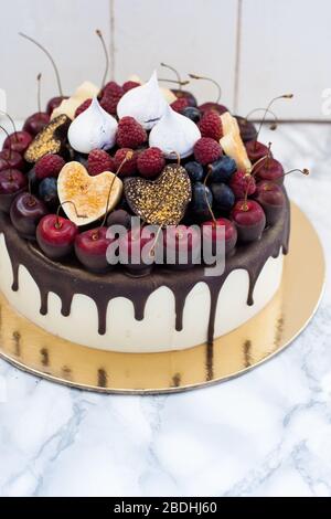 Vanillekäsekuchen mit geschmolzener dunkler Schokolade, frischen Beeren, Kirschen, Schokoladenherzen und Baiser. Weißer rustikaler Hintergrund. Stockfoto