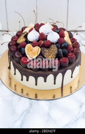 Vanillekäsekuchen mit geschmolzener dunkler Schokolade, frischen Beeren, Kirschen, Schokoladenherzen und Baiser. Weißer rustikaler Hintergrund. Stockfoto