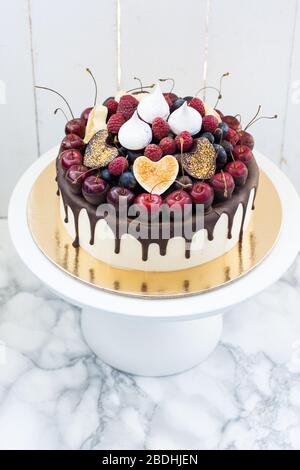 Vanillekäsekuchen mit geschmolzener dunkler Schokolade, frischen Beeren, Kirschen, Schokoladenherzen und Baiser. Weißer rustikaler Hintergrund. Stockfoto
