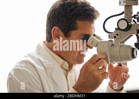 Männlicher Arzt suchen nach etwas durch ein Mikroskop. Stockfoto