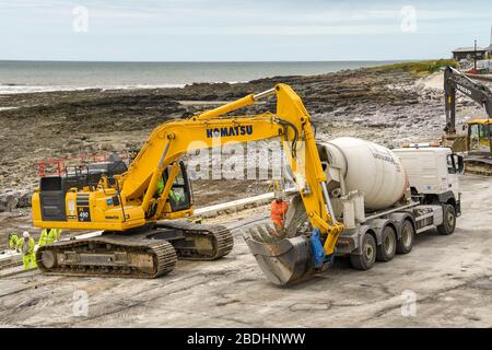 PORTHCAWL, WALES - JUNI 2018: Betonmischer, der den fertigen Mischbeton in den Eimer eines Schwerlastbaggers für die Abwehrkräfte entlädt Stockfoto