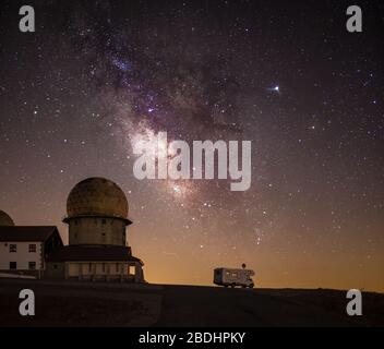 Sternenhimmel mit Milchstraße, die über Sternwarte und Wohnmobil auf Bergstraße leuchtet Stockfoto