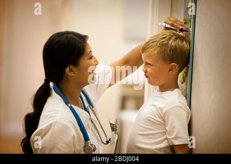 Kleiner Junge, der seine Körpergröße von der Krankenschwester messen ließ. Stockfoto