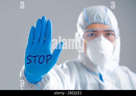 COVID-19-Konzept. Asiatischer Mann in Schutzanzug macht Schild mit Hand mit Aufschrift Anschlag Stockfoto