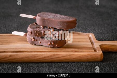 Schokoladenbedeckte Vanilleeissägel auf dem Holzbrett Stockfoto