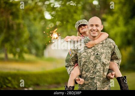 Lächelnd männlichen Soldaten piggy-backing seine junge Tochter in ihrem Hinterhof. Stockfoto