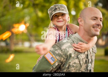 Lächelnd männlichen Soldaten piggy-backing seine junge Tochter in ihrem Hinterhof. Stockfoto