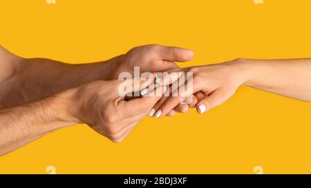 Junger Kerl, der den Verlobungsring mit einem großen Diamanten auf die Hand seines Verlobten setzt, orangefarbener Hintergrund. Panorama Stockfoto