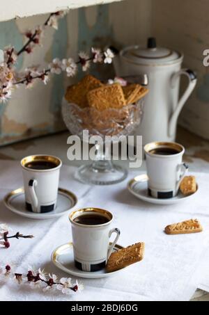 Kaffee serviert mit Shortbread-Keksen und Süßigkeiten im Hintergrund von blühenden Zweigen und einem alten Schrank. Stockfoto