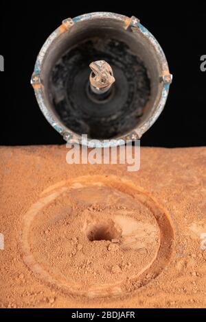 Bohren eines großen Lochs in rotem Backstein. Bauarbeiten in der Heimwerkstätte. Dunkler Hintergrund. Stockfoto