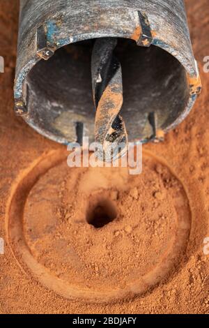 Bohren eines großen Lochs in rotem Backstein. Bauarbeiten in der Heimwerkstätte. Dunkler Hintergrund. Stockfoto