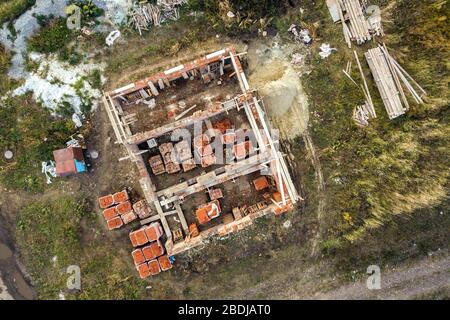 Luftbild der Baustelle für zukünftiges Ziegelhaus, Betonfundament und Stapel gelber Lehmziegel für den Bau. Stockfoto