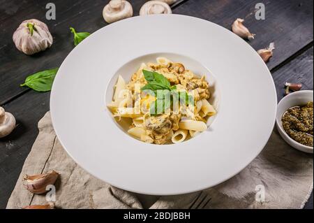 Nahaufnahme der Penne in großen weißen Platten mit Spinatblättern und Knoblauch auf einem dunklen Holztisch. Traditionelle mediterrane Küche Stockfoto