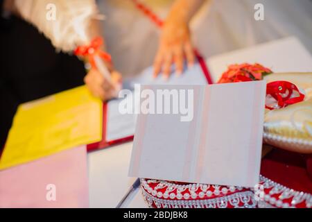 Die in einem Hochzeitskleid untersetzende Frau schließt sich dem Vertrag an. Hände von kaukasischen Hochzeitsleuten, die das Dokument bei der Zeremonie unterschreiben, Nahansicht Stockfoto