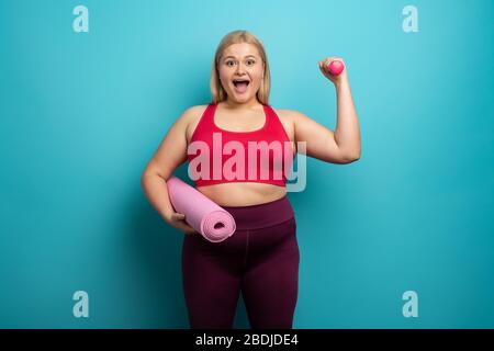 Fat Girl macht zu Hause Fitness-Studio. Zufriedener Ausdruck. Hintergrund Zyan Stockfoto