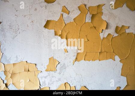 Alte verputzte Wand mit teilweise abblätternden und rissiger gelber Farbe. Stockfoto