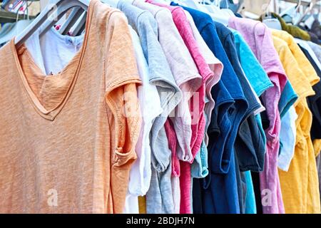 T-Shirts in verschiedenen Farben in einer Reihe. Im Sommer werden in einem Einzelhandelsgeschäft bunte Frauen-T-Shirts in Pastelltönen an Kleiderbügeln getragen. Stockfoto