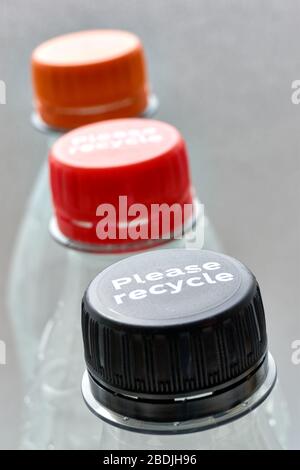 Plastikflaschen und schwarze, orange und rote Flaschenverschlüsse mit Please recycle-Meldung vor grauem Hintergrund. Konzept der Plastikverschmutzung. Stockfoto