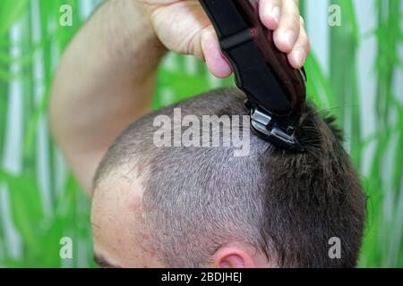 Der Kerl schneidet sich mit einer Schreibmaschine die Haare. Haarschnitt zu Hause mit einem speziellen Haarschneider. Stockfoto