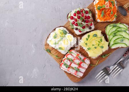 Sechs Sandwiches auf Toast mit frischen Karotten, Gurken, Ananas, rotem Currant, Krabbenstäbchen und Wachteleiern mit Erbsen Mikrogrün auf Holzbrett Stockfoto