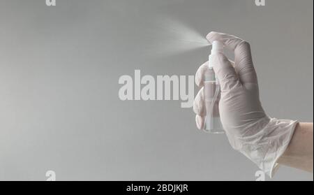 Einweghandschuhe mit Alkoholsprühflasche auf grauem Hintergrund mit Kopierraum einziehen Stockfoto