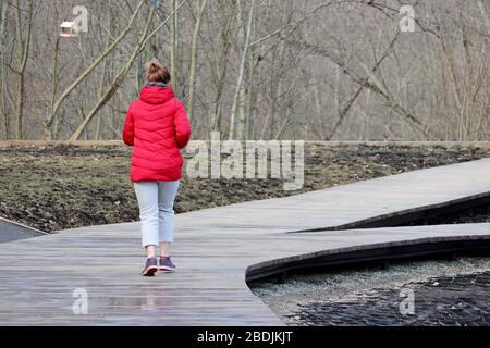 Mädchen in roter Daunenjacke im Federpark, Rückansicht. Konzept des Trainings, Frau Läuferin, Schlankheitskinder in der kalten Jahreszeit Stockfoto