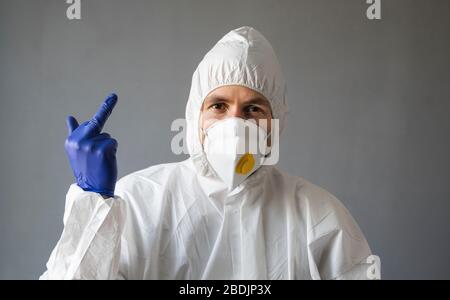 Der Arzt in weißem Schutzanzug, medizinischer Maske und Gummihandschuhen zeigt dem Virus Mittelfinger. Hilfe für Menschen während einer Coronavirus-Pandemie Stockfoto