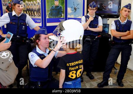 Eine Polizistin hilft einem Kind, während der Feier des Belgischen Nationalfeiertags einen Polizeihelm in der Ausstellung der Polizei und der Strafverfolgungsbehörden auszuprobieren.Brüssel.Belgien Stockfoto