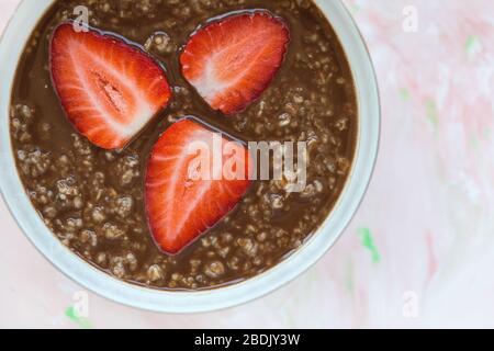 SchokoladenHaferbrei Haferbrei und Erdbeeren Frühstück in Schüssel auf pinkfarbenem Hintergrund, Konzept des gesunden Essens veganer Speisen. Nahaufnahme, selektiver Fokus Stockfoto