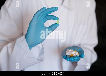 Viele kleine weiße Pillen in den Händen eines Arztes, der medizinische blaue Einweghandschuhe trägt. Hände nehmen eine Tablettenform. Stockfoto