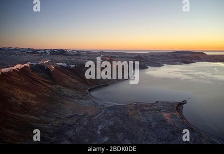 Wundervolle Sonnenuntergangslandschaft von rauer Felsküste mit ruhigem Wasser gegen den wolkenlosen bunten Himmel in Island Stockfoto