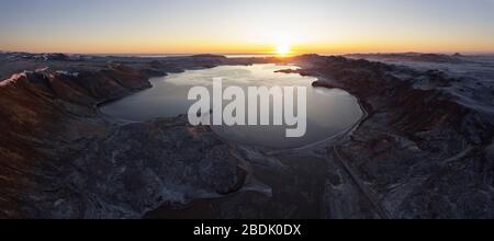 Spektakuläre nordische Panoramalandschaft mit ruhigem See, umgeben von unwegsamem, felsigem Gelände gegen klaren Himmel mit Sonne über Horizont in Island Stockfoto