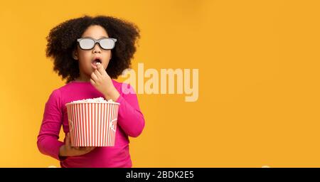 Kinderkino. Schwarzes kleines Mädchen, das 3D-Brille trägt und Popcorn isst Stockfoto