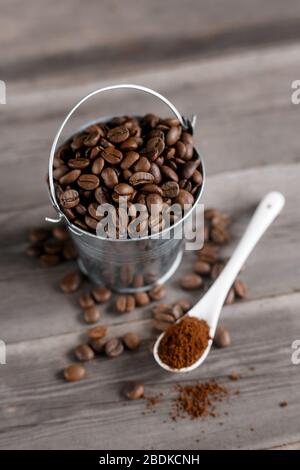 Arabica-Kaffeebohnen in einem kleinen kleinen kleinen Eimer. Gemahlener Kaffee in einem weißen Keramiklöffel auf Holzgrund Stockfoto