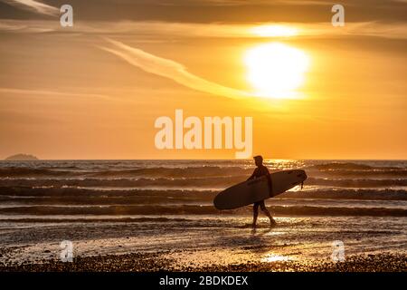 Ein Mann mit einem Surfbrett spaziert am Polzeath-Strand an der Nordküste Cornwalls während des Sperrens von Coronavirus entlang. Stockfoto