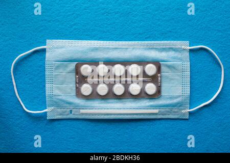 Viele medizinische Maske, medizinische Schutzmaske auf blauem Hintergrund mit mehrfarbigen Tabletten. Die einmal-OP-Gesichtsmaske deckt Mund und Nase ab. Konzept für das Gesundheitswesen und die Medizin. Stockfoto