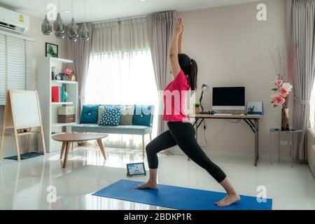 Asian Woman macht Yoga-Übungen, um Schritt für Schritt von ihren Computern zu entfernt, um halbtägige Trainingsunterbrechungen über Livestream-Videos auf digitalen Tablets zu machen d Stockfoto