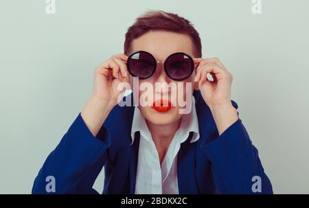 Portrait closeup überraschte junge Frau in einer runden Sonnenbrille über grüngrauem Hintergrund. Angry Girl Business Blue marineblaue Anzug, weißes Hemd Stockfoto