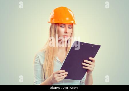 Architektendenken. Nahaufnahme Portrait ernste junge Baufrau mit gelber Kappe erwägt die Lageplanung, auf Notizblock isoliert gr hinunterzuschauen Stockfoto