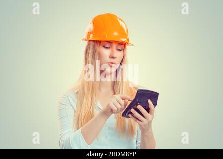Architekten, die Ausgaben berechnen. Nahaufnahme Portrait Serious Construction Woman, Yellow Cap Pondering Situation Planning Calculator in hands isolated GREE Stockfoto