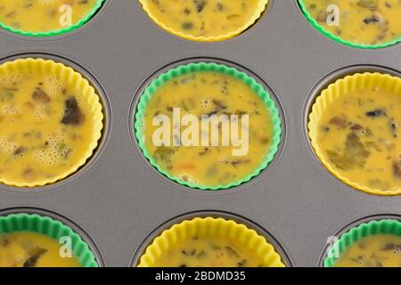 Ungekochte Rühreibecher mit gehackten Pilzen, Paprika und Zwiebeln in Silikon-Muffin-Tassen auf Muffin-Backform Stockfoto